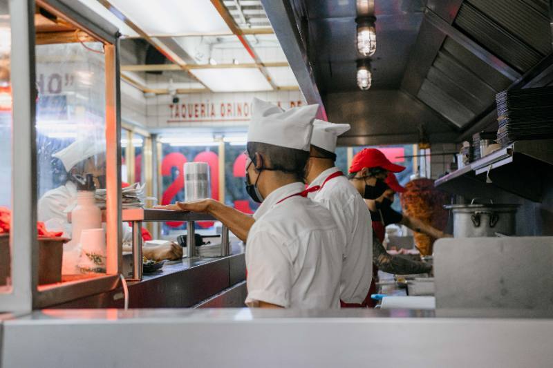 Ilustrasi pemilik bisnis kuliner sedang menghitung proporsi biaya sewa ruko, biaya renovasi, gaji karyawan, dan HPP bahan baku menggunakan kalkulator bisnis.